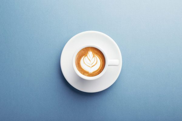 A cup of coffee with latte art. A cup of cappuccino with beautiful latte art on blue background. Top view, central composition.