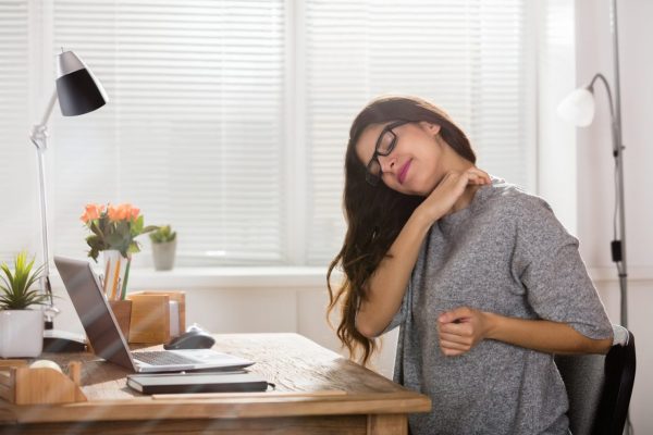 Businesswoman Having Neck Pain Woman rubbing her sore shoulders while working at a desk