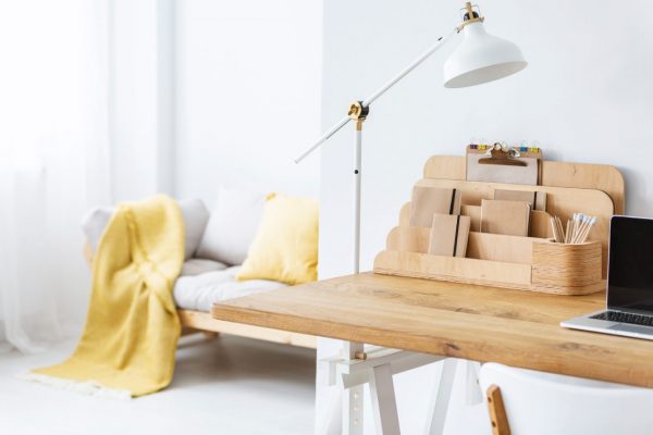 White lamp on wooden desk with laptop in bright freelancer’s interior with organizer. Real photo Wooden desk set up in spacious home