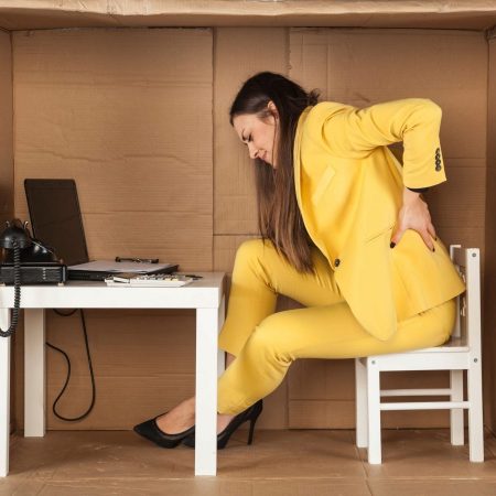 Woman with back pain sitting at a desk set up in a cardboard box